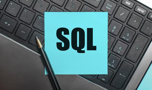 On the computer keyboard there is a pen and a blue sticker with the text sql